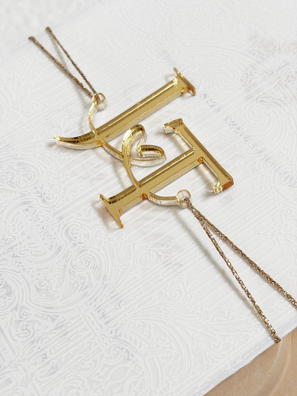 Gold mirror lettering "M" and "O", are connected by a thin, gold-colored string.  The card is decorated with gold foil floral motif.