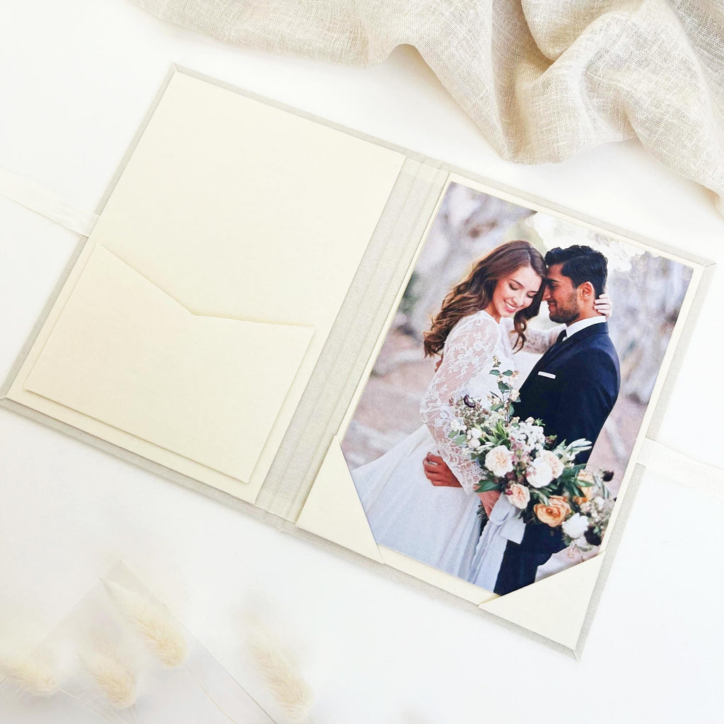 A cream linen wedding invitation folio with a gold foil monogram "P & T"  is tied with a grosgrain bow.